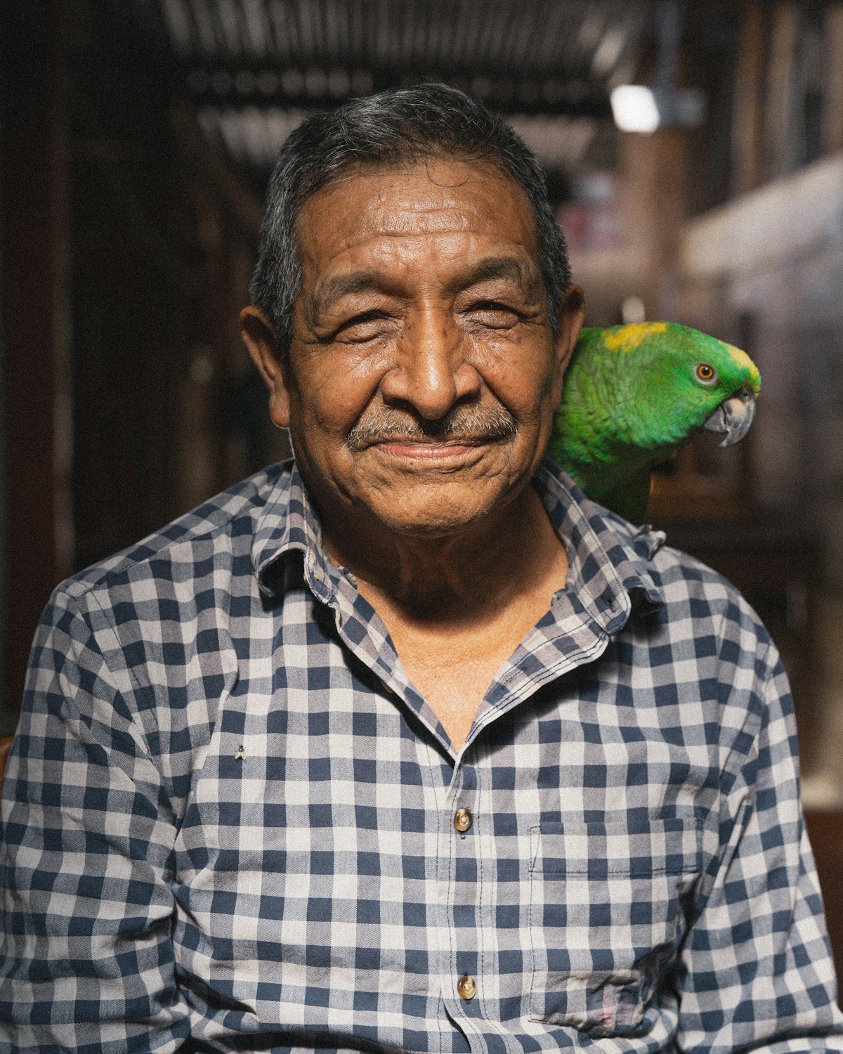 A smiling older man with a green parrot perched on his shoulder.